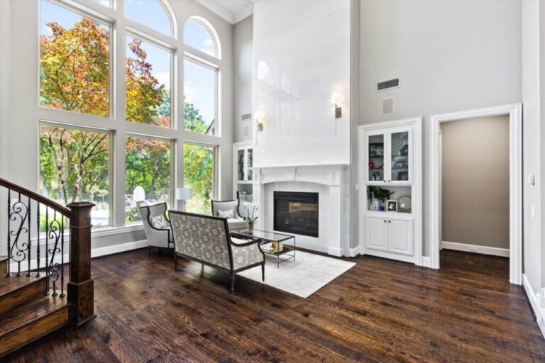 Interior living room in Frisco, Texas with premium dark wooden flooring, large arched windows, white fireplace wall, and modern luxury décor.