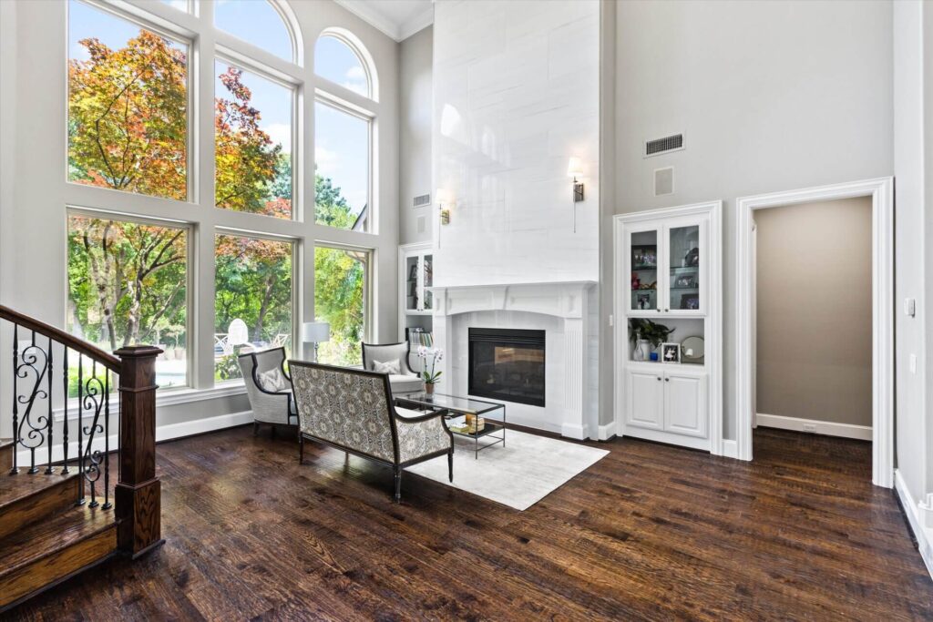 Interior living room in Frisco, Texas with premium dark wooden flooring, large arched windows, white fireplace wall, and modern luxury décor.